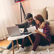 Man and woman couple sitting on living room floor, looking over documents